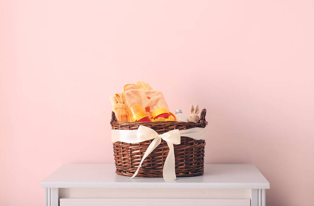 Wicker basket with gifts for baby on light background